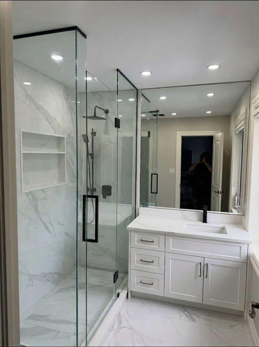 Marble-tiled shower with black hardware beside a white shaker vanity